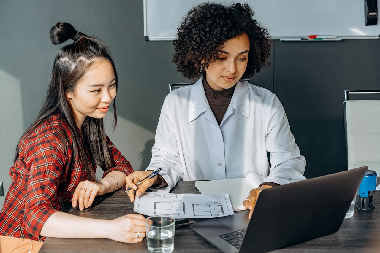 Two women working together on a laptop in a modern office setting for teamwork project.